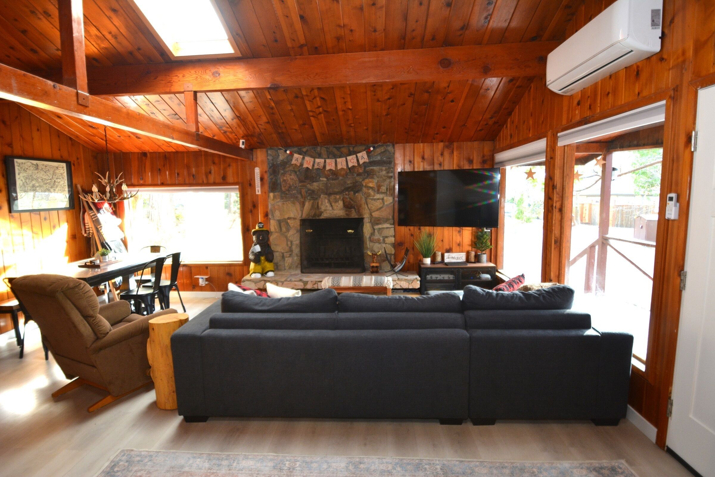 A cozy living room with a large sectional sofa, a stone fireplace, and wooden walls.