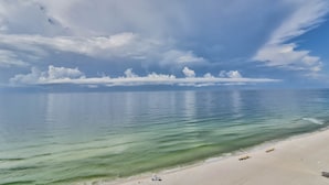 A beach with clear turquoise water, a sandy shore, and a partly cloudy sky. - Romar Tower Condos (Orange Beach)