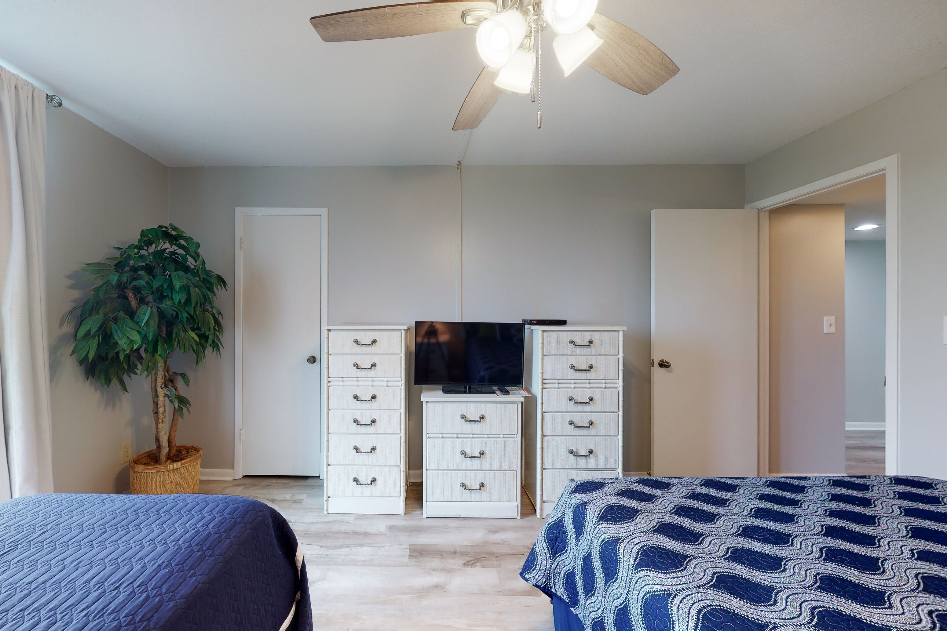 Ein Schlafzimmer mit Deckenventilator, Fernseher, Zimmerpflanze und zwei Betten mit gemusterten Bettdecken.