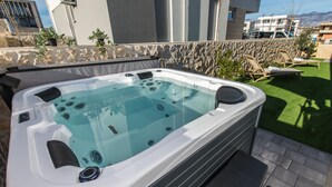 Ein Whirlpool mit Steinwand, Sitzgelegenheiten im Freien und Blick auf Gebäude und Berge.