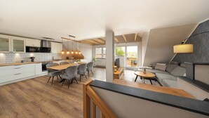 Una cocina moderna con suelo de madera, armarios blancos y un comedor con sillas grises.