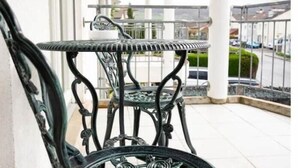 A metal outdoor table and chair set on a balcony with a white railing and a view of a residential street. - Ferienhaus Marina (Weil am Rhein)