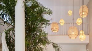 Un interior amplio con escalera, una planta grande en maceta, mobiliario de mimbre y varias luces colgantes.