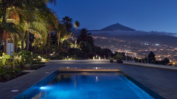 Piscina con vista a un paisaje urbano y una montaña al anochecer.