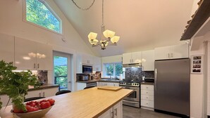A modern kitchen with white cabinets, a wooden island, stainless steel appliances, and a large window providing natural light. - Availability limited to Winter 2027 (from January 15th to March 13th, 2027) short or long term 2 months, for a serene escape in the heart of the Laurentians. (Prévost)