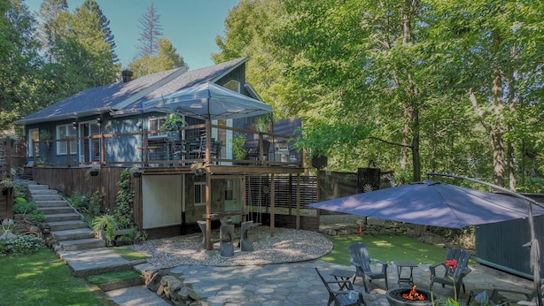 A two-story house with a covered patio area, stone steps leading to the entrance, and a fire pit with seating. - Availability limited to Winter 2027 (from January 15th to March 13th, 2027) short or long term 2 months, for a serene escape in the heart of the Laurentians. (Prévost)