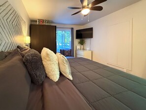 A bedroom with a bed, pillows, a ceiling fan, a TV, and a window with a view of the outdoors. - Available exclusively for Winter 2027, from January 15 to March 13. Short or long stays for a peaceful getaway in the heart of the Laurentians. (Prévost)