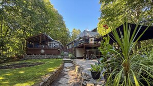 A stone pathway leading to a wooden cabin with a covered porch, surrounded by lush greenery and trees. - Availability limited to Winter 2027 (from January 15th to March 13th, 2027) short or long term 2 months, for a serene escape in the heart of the Laurentians. (Prévost)