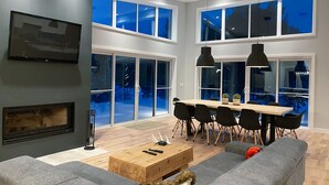 A modern living room with a fireplace, a dining area with a table and chairs, and large windows offering a view of the outdoors. - Magnificent chalet with a contemporary design: dream location for an unforgettable holiday (Notre-Dame-de-la-Merci)