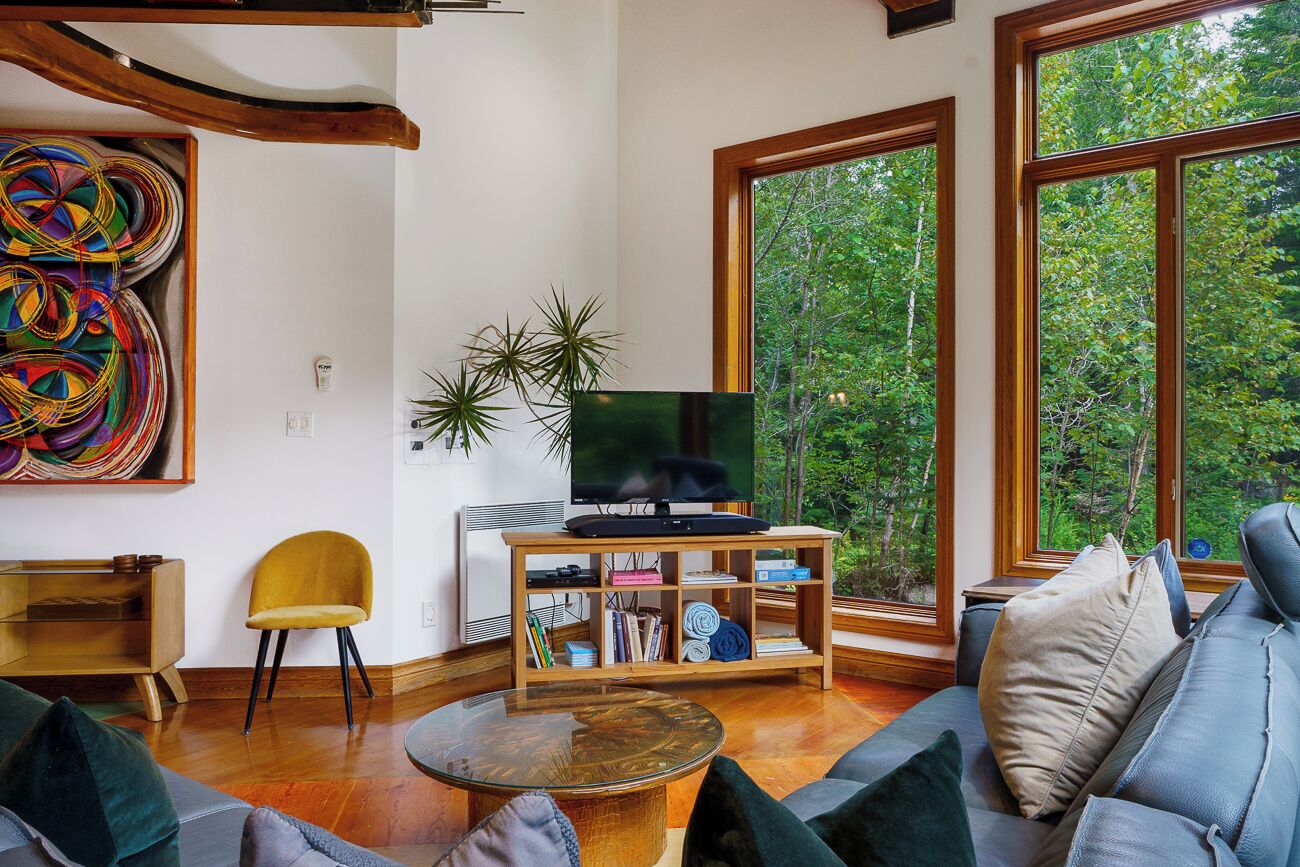 Ein modernes Wohnzimmer mit einem großen Fernseher auf einem Holzständer, einem Sofa, einem gelben Sessel und einem Bücherregal.