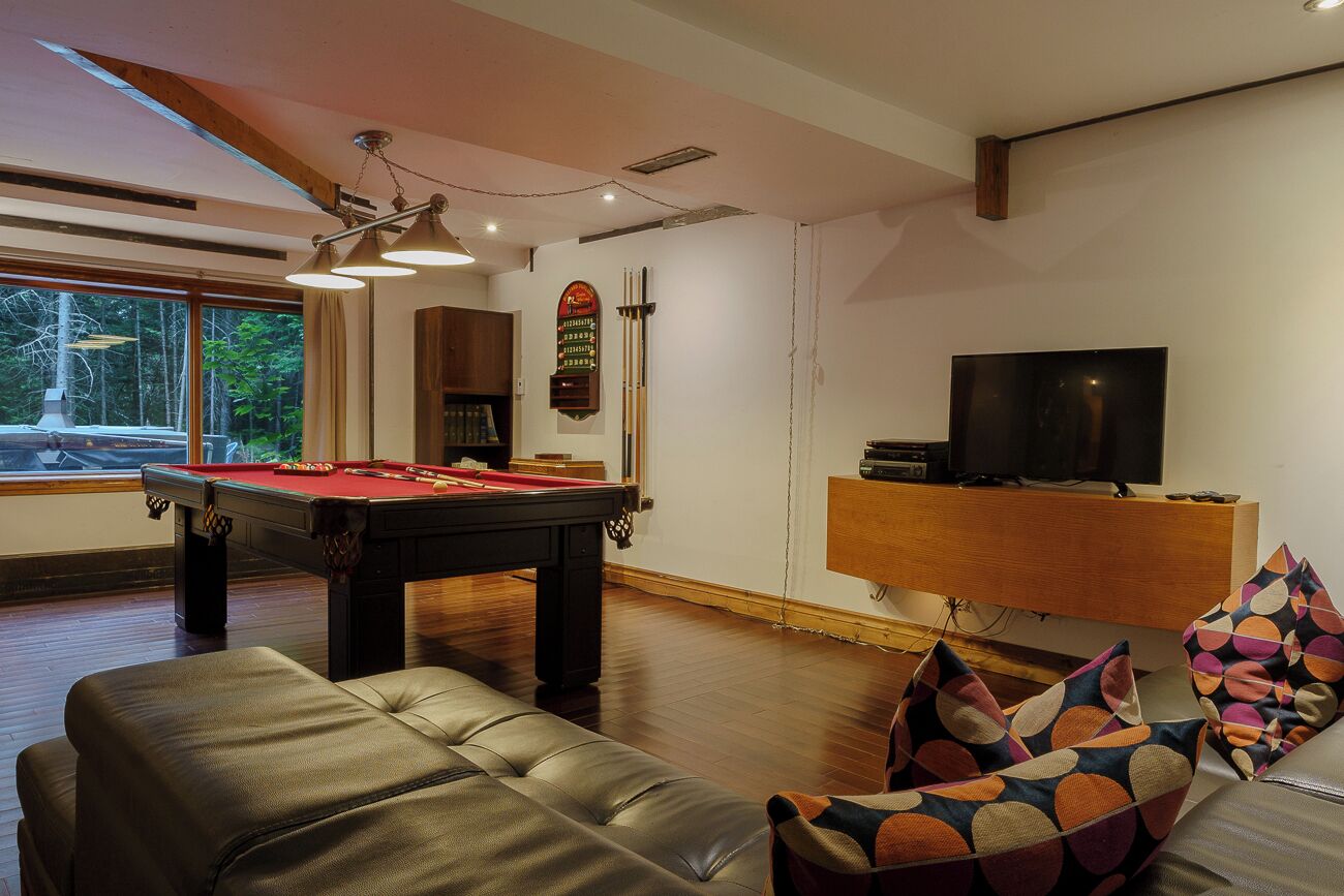 Una sala de estar moderna con mesa de billar, un sofá con cojines estampados, televisor y mueble de madera.
