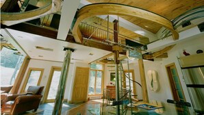 A spacious interior with a glass staircase, wooden beams, and a high ceiling.