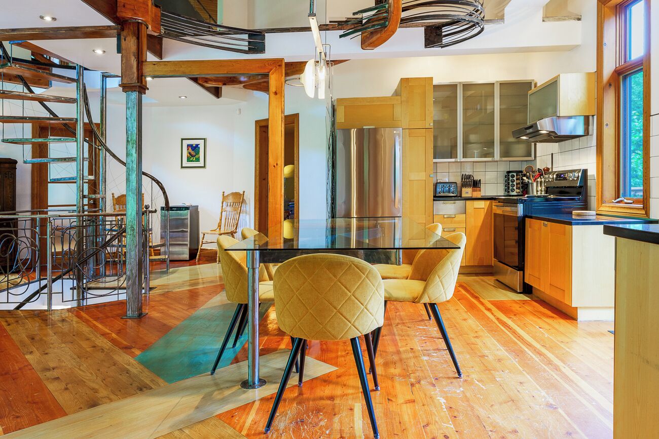 A modern kitchen with a glass dining table, yellow chairs, and stainless steel appliances.