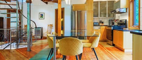 A modern kitchen with a glass dining table, yellow chairs, and stainless steel appliances.