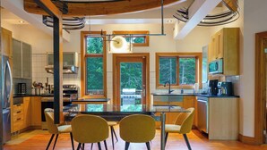 A modern kitchen with wooden cabinets, a central island, and large windows offering a view of the outdoors.