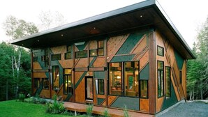 A modern, multi-story cabin with a geometric facade, large windows, and a sloped roof.