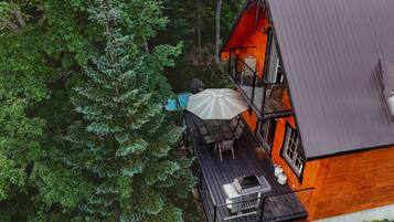 A wooden deck with a grill, outdoor table, and umbrella, surrounded by dense forest.