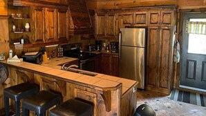 A rustic kitchen with wooden cabinets, a stainless steel refrigerator, and a central island with bar stools. - Super cute cedar chalet surrounded by the forest with access to water (Entrelacs)