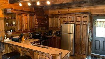 A rustic kitchen with wooden cabinets, a stainless steel refrigerator, and a central island with bar stools.
