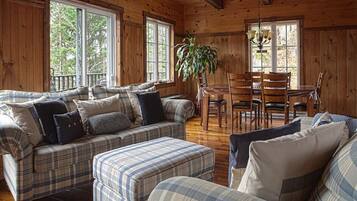 A cozy cabin interior with plaid-patterned furniture, a dining area, and large windows.