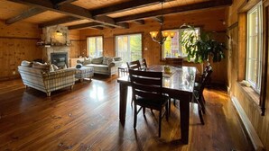 A spacious log cabin interior with a dining area, a fireplace, and a large window providing natural light. - Super cute cedar chalet surrounded by the forest with access to water (Entrelacs)