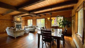 A spacious log cabin interior with a dining area, a fireplace, and a large window providing natural light.