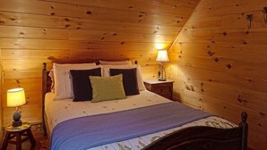 A wooden-paneled bedroom with a bed, two bedside tables, and lamps. - Super cute cedar chalet surrounded by the forest with access to water (Entrelacs)