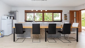 Una cocina moderna con una isla central, sillas negras, un refrigerador blanco y un ventanal con vistas a árboles.