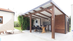 Un patio techado con una mesa y sillas, un muro de ladrillo y una estructura de madera.
