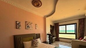Een hotelkamer met een groot bed, een bureau, een stoel en uitzicht op het strand door het raam.
