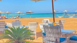 Een strand met witte parasols en rieten ligstoelen.