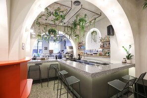 A bar area with a counter, bar stools, hanging plants, and shelves with bottles. -  Next door Athens  (Athens)