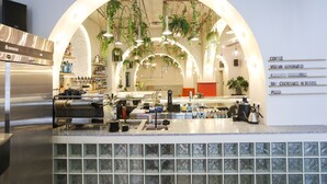 Un café moderno con zona de bar, máquinas de espresso y una pizarra de menú que ofrece café, affogato vegano, proteínas saludables, cócteles, cervezas y pizza.