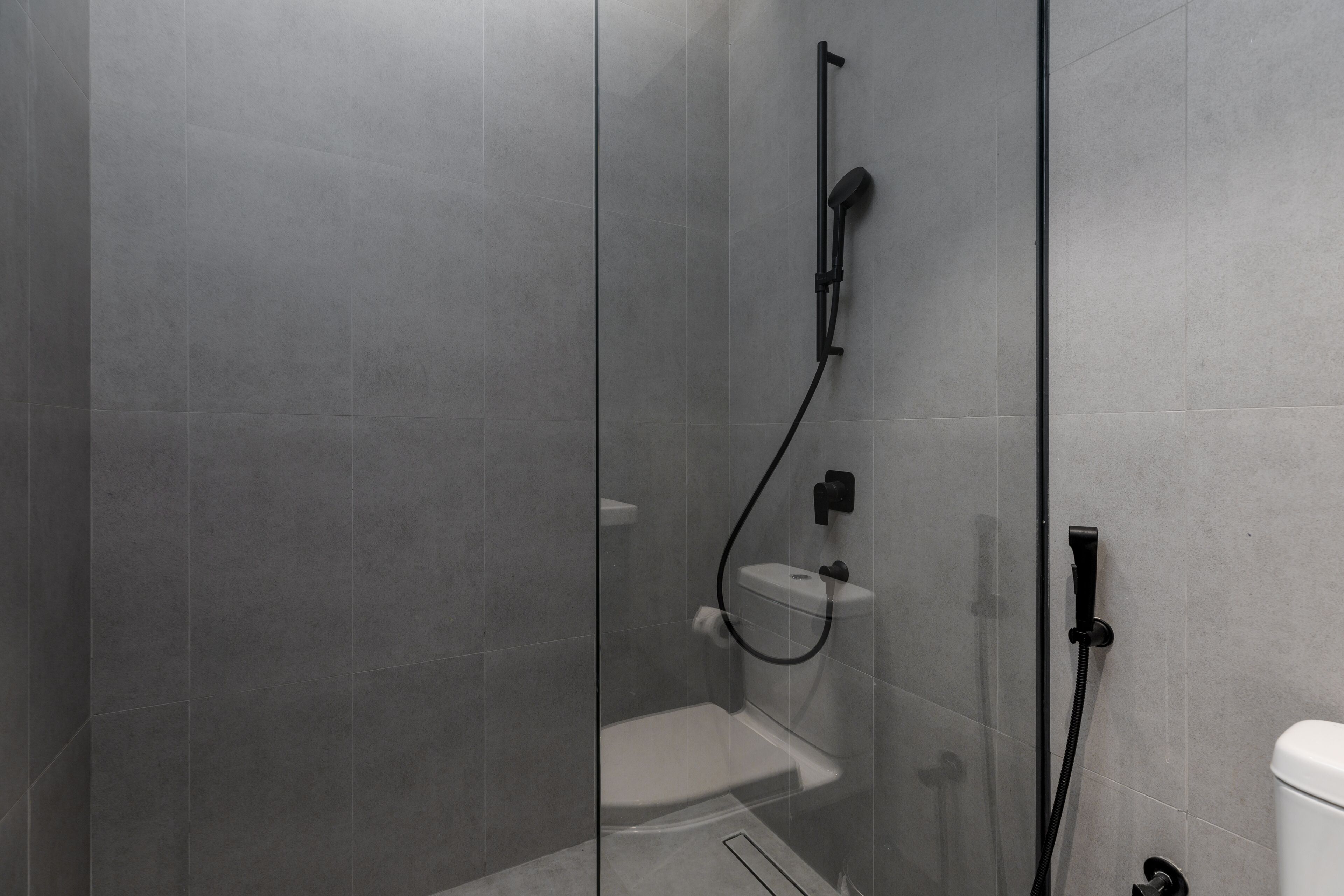 A modern bathroom with a glass-enclosed shower, a white toilet, and a black faucet.