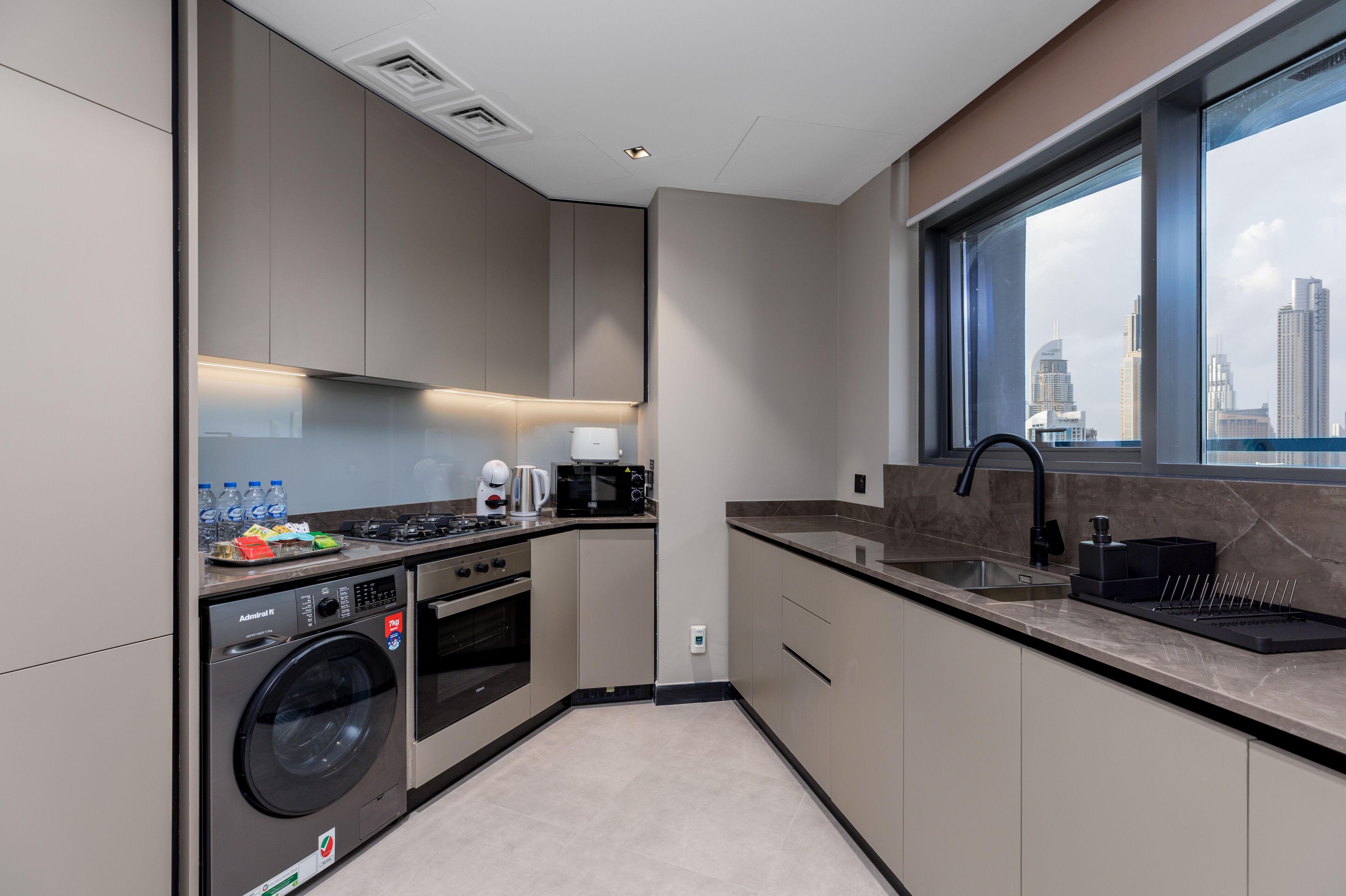 A modern kitchen with built-in appliances, a large window with a city view, and a compact layout.