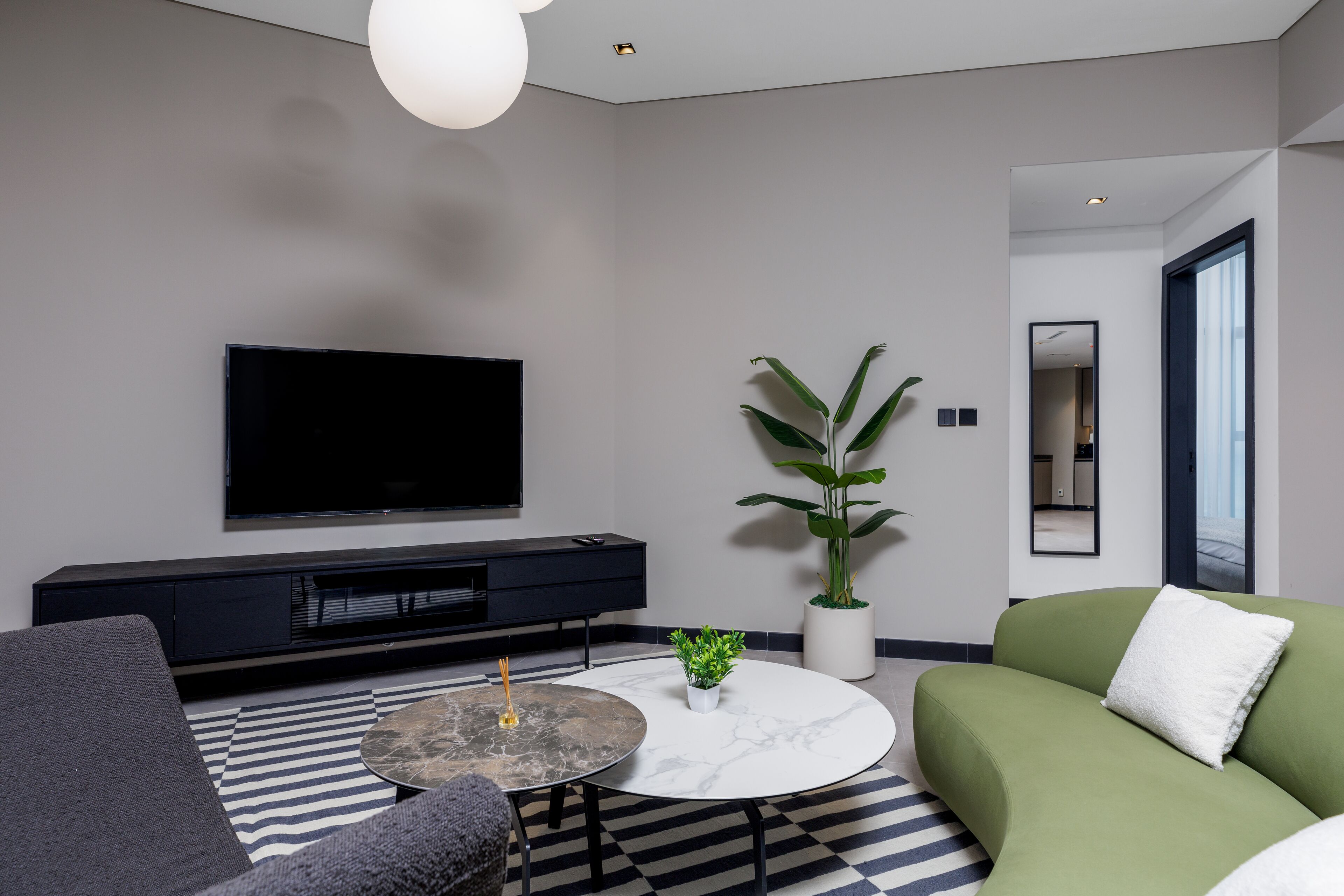 A modern living room with a flat-screen TV, a round coffee table, a sofa, and a potted plant.