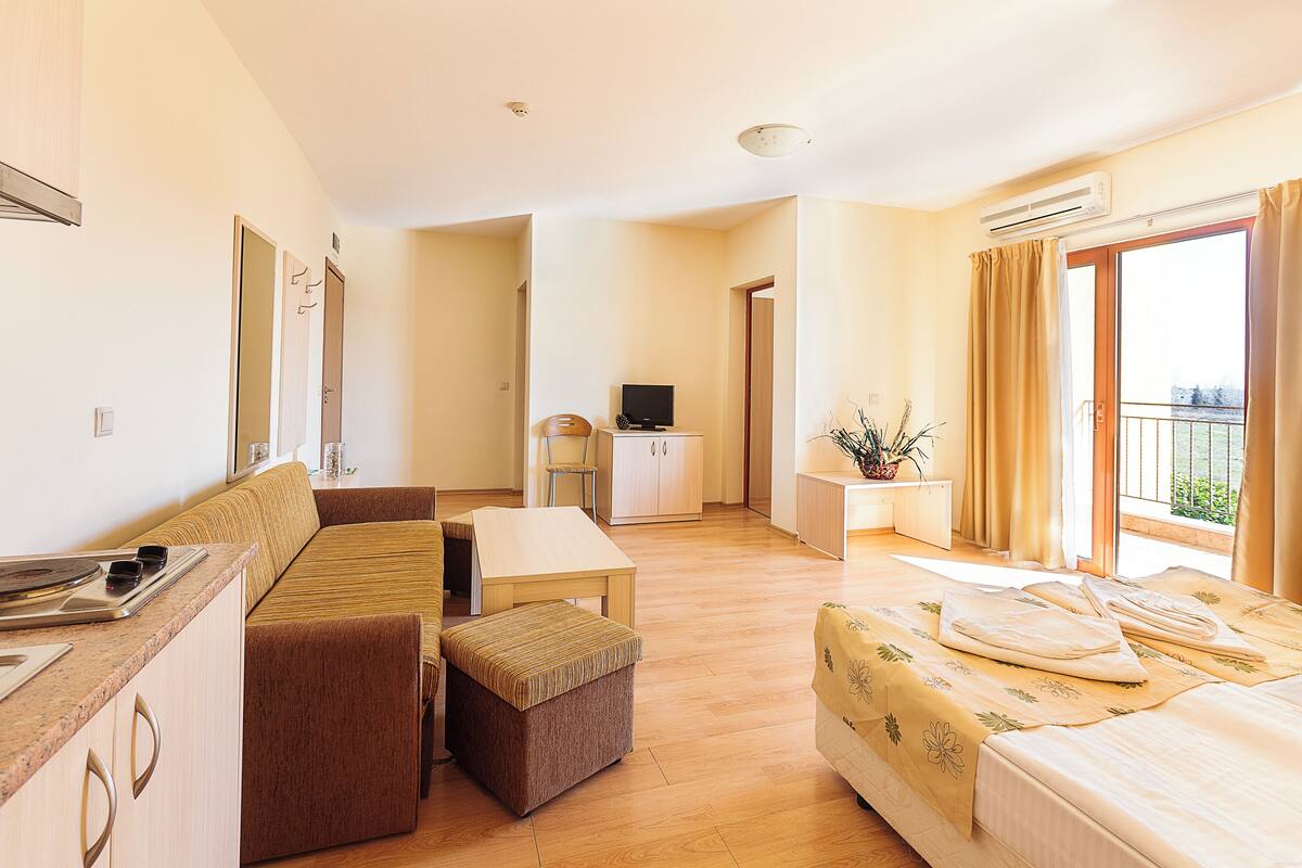 Een hotelkamer met een bank, een eettafel, een televisie, een balkon met gordijnen en een airconditioning.