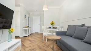 Una sala de estar moderna con un sofá gris, una mesita redonda, una zona de comedor blanca y un televisor montado en la pared.