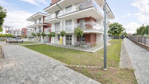 Un moderno edificio residencial de varios pisos con balcones, un camino pavimentado y un césped bien cuidado.