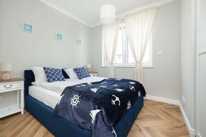 A bedroom with a bed, a nightstand, a window with curtains, and a wall with three small pictures. - Sunny Apartment | SPA and 100 m to the Beach (Rewal)