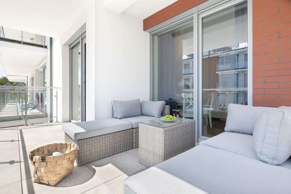 Ein moderner Balkon mit Korbmöbeln, einer Glastür und Blick auf die Stadt.