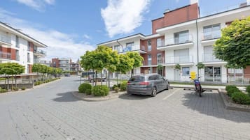 Um moderno conjunto de apartamentos com estacionamento pavimentado, carros estacionados e uma motocicleta.