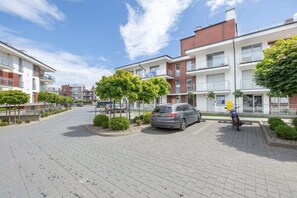 Un immeuble d’appartements moderne avec une allée pavée, des voitures garées et une moto.