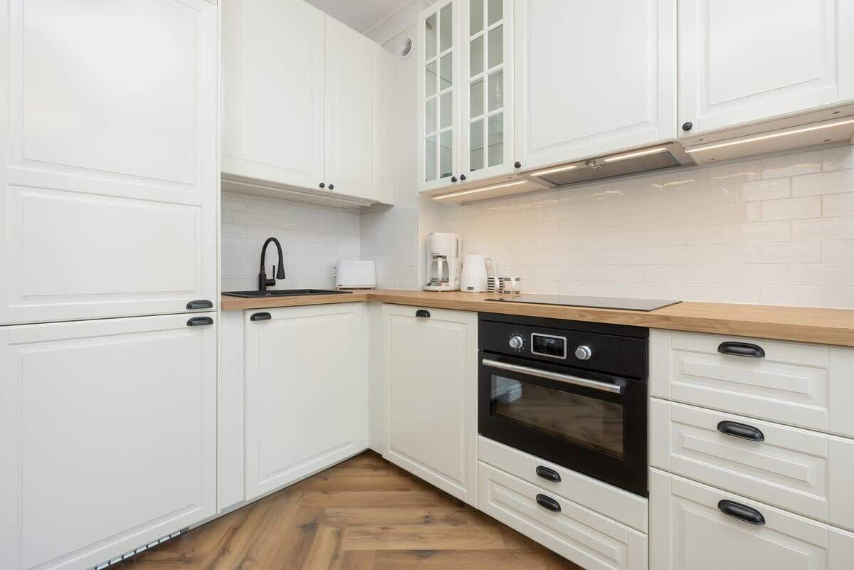 Une cuisine moderne avec des meubles blancs, un plan de travail en bois et un four noir.