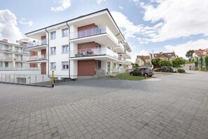 A multi-story residential building with balconies, a paved driveway, and a parked car.