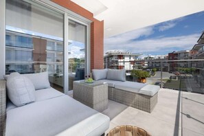Un balcon doté de meubles en osier, d’une porte vitrée et offrant une vue sur les immeubles voisins.