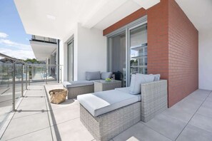 Eine moderne Terrassengestaltung mit Korbmöbeln und einer Glastrennwand.
