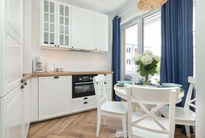 A modern kitchen with white cabinets, a built-in oven, and a dining area with white chairs and a table.