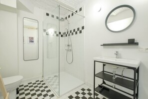 Une salle de bain moderne avec une douche à parois de verre, un lavabo blanc doté d’un cadre noir et un carrelage à motifs géométriques.