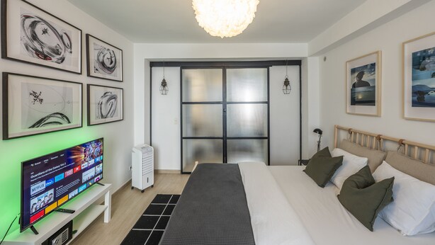 A modern hotel room with a large bed, a flat-screen TV, artwork on the walls, and a large window with a view. - Boutique Duplex in Brussels - Superb Location (Molenbeek-Saint-Jean)